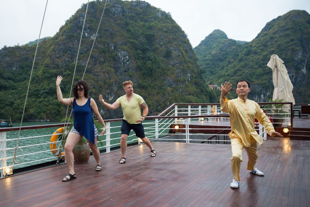 Relaxing Tai Chi session on a cruise deck with lush green mountains in Vietnam's Ha Long Bay.