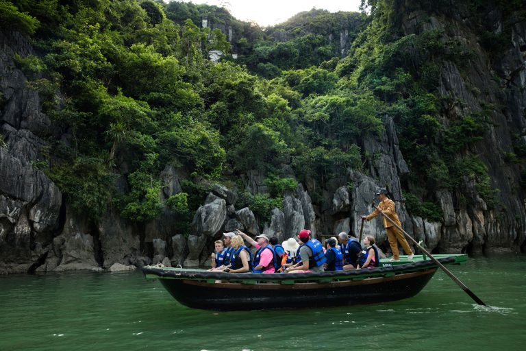 Boat tour through Ha Long Bay with tourists exploring limestone karsts, lush greenery, and emerald waters in Vietnam.