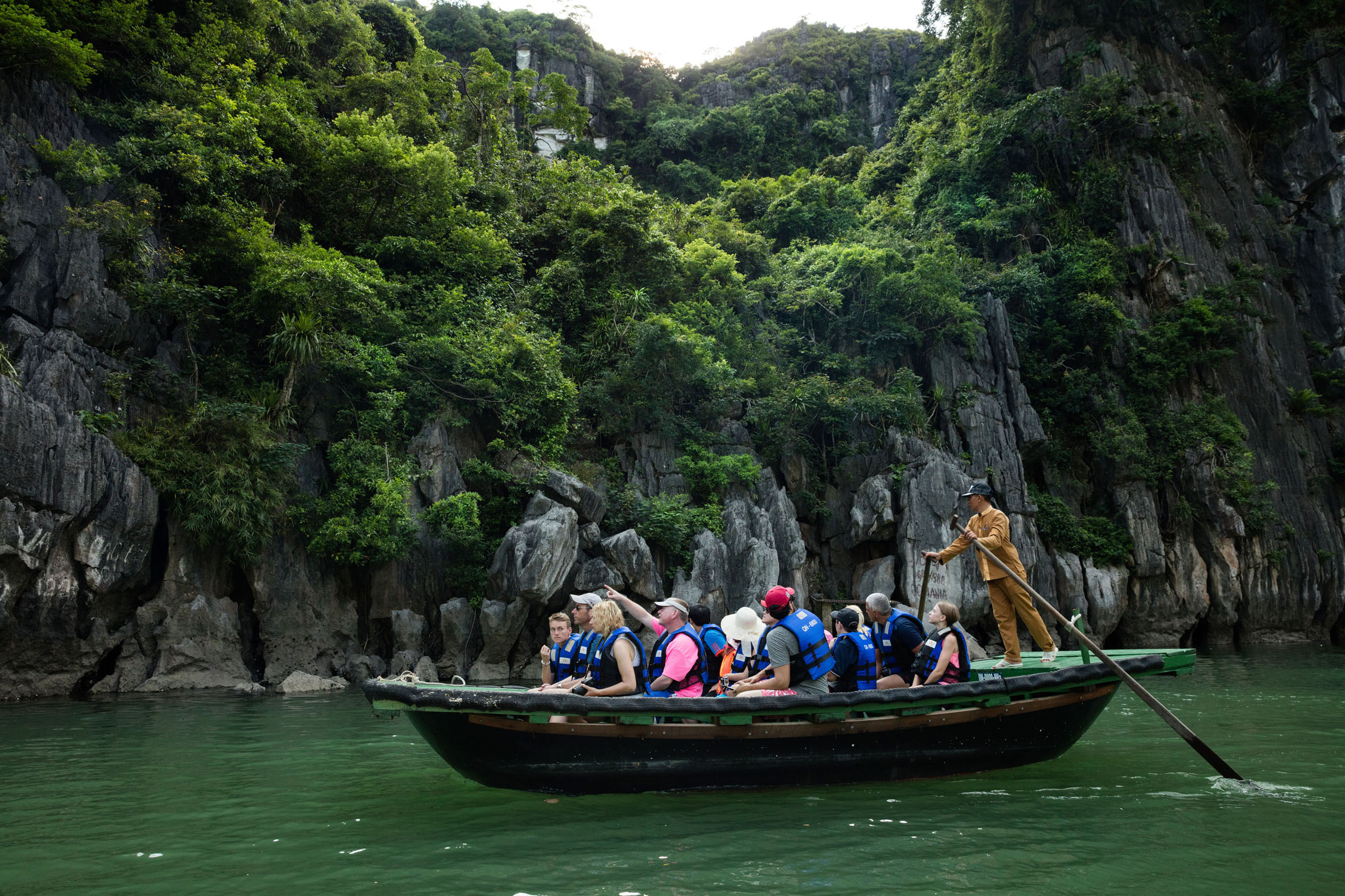 Boat tour through Ha Long Bay with tourists exploring limestone karsts, lush greenery, and emerald waters in Vietnam.