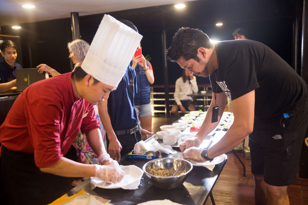 Chef in traditional outfit and a man preparing food at a Vietnamese cuisine cooking class.
