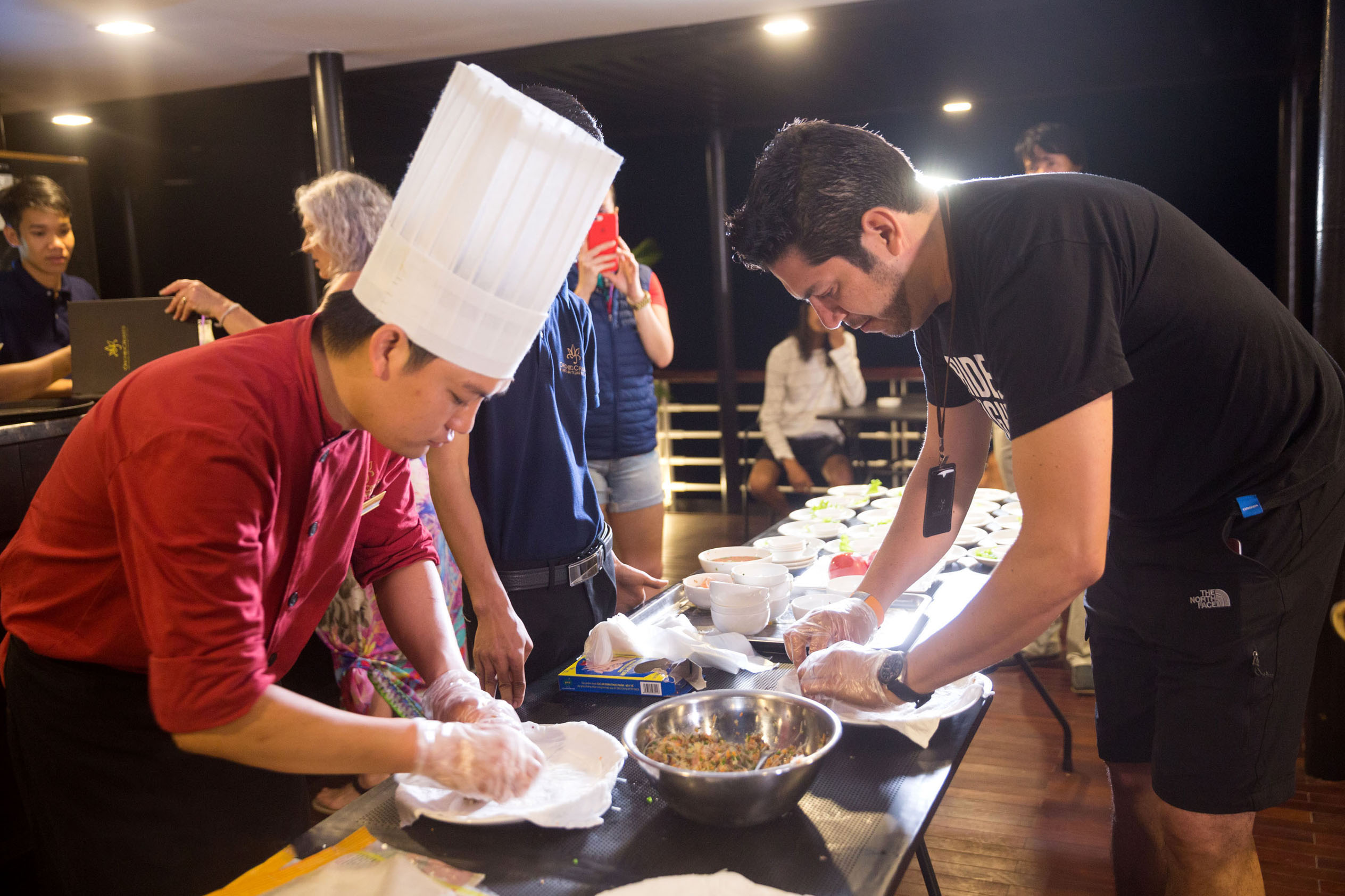 Chef in traditional outfit and a man preparing food at a Vietnamese cuisine cooking class.