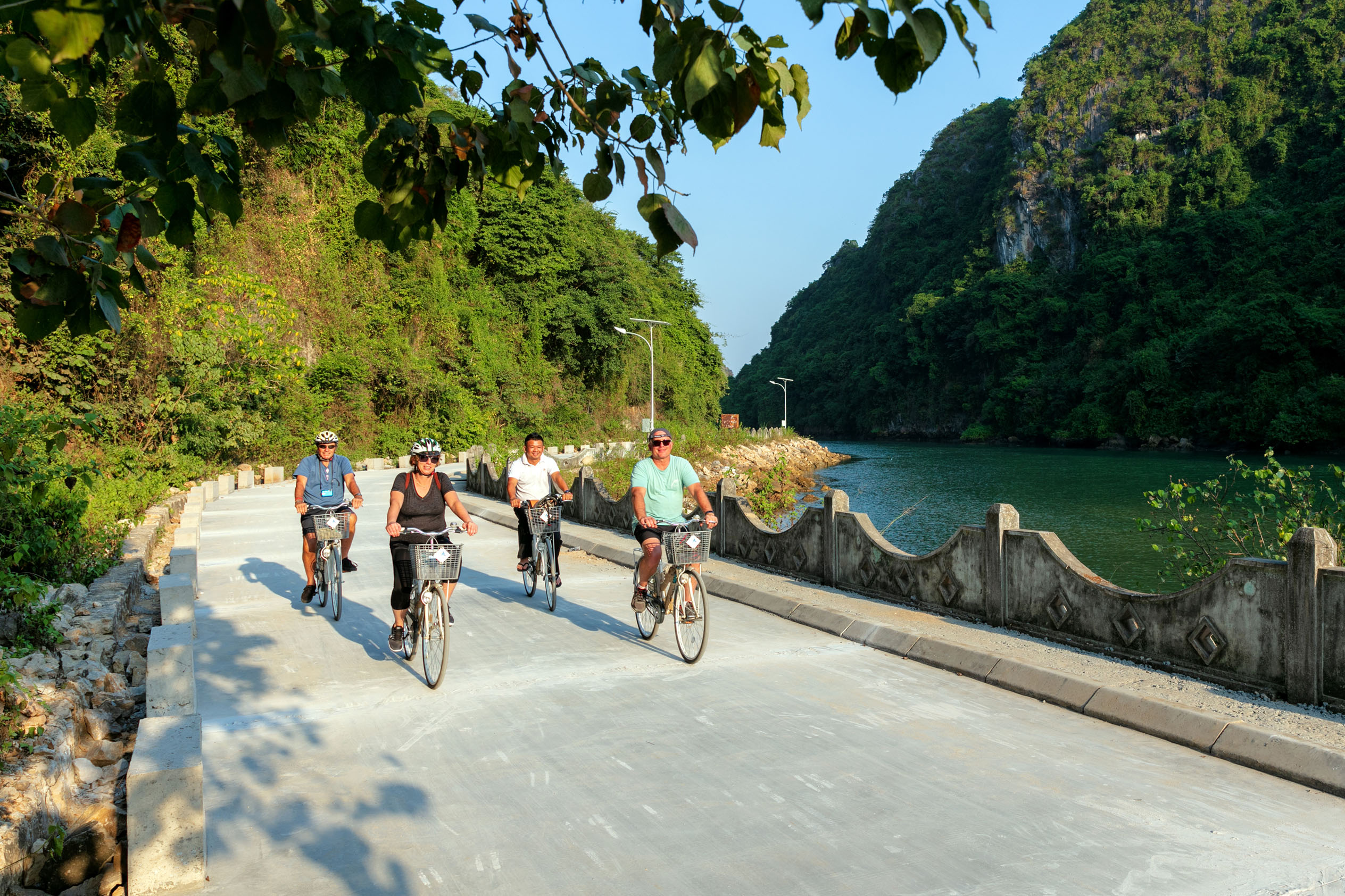 Cyclists riding along a scenic river route surrounded by lush green mountains in Vietnam.