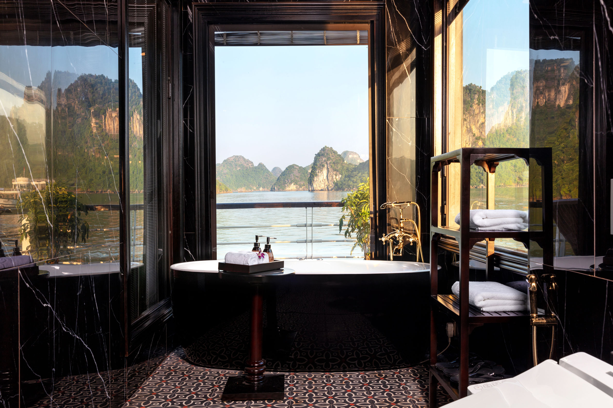 Luxurious hotel bathroom with river and mountain view, bathtub, elegant black marble decor, and modern fixtures.