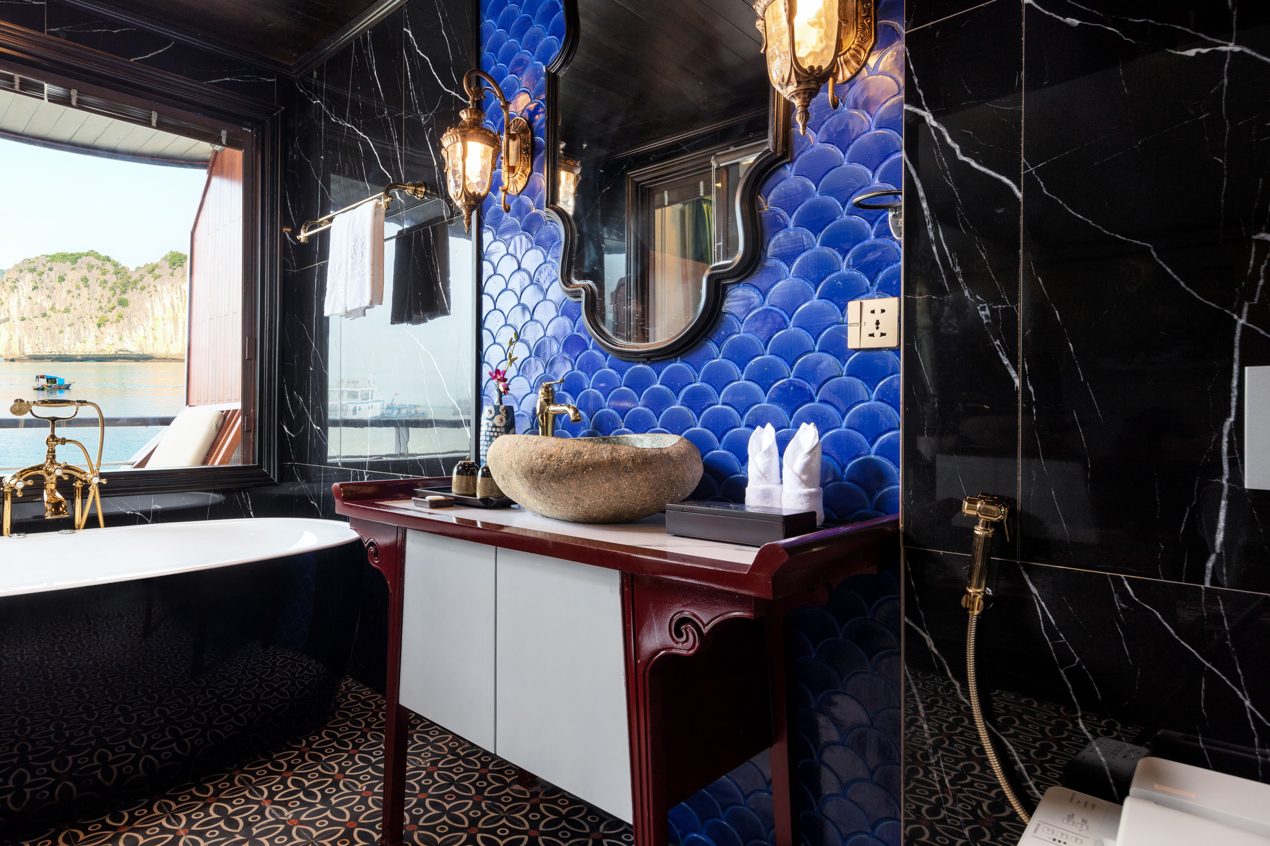 Luxurious bathroom with blue scale tiles, elegant gold fixtures, and scenic ocean view.
