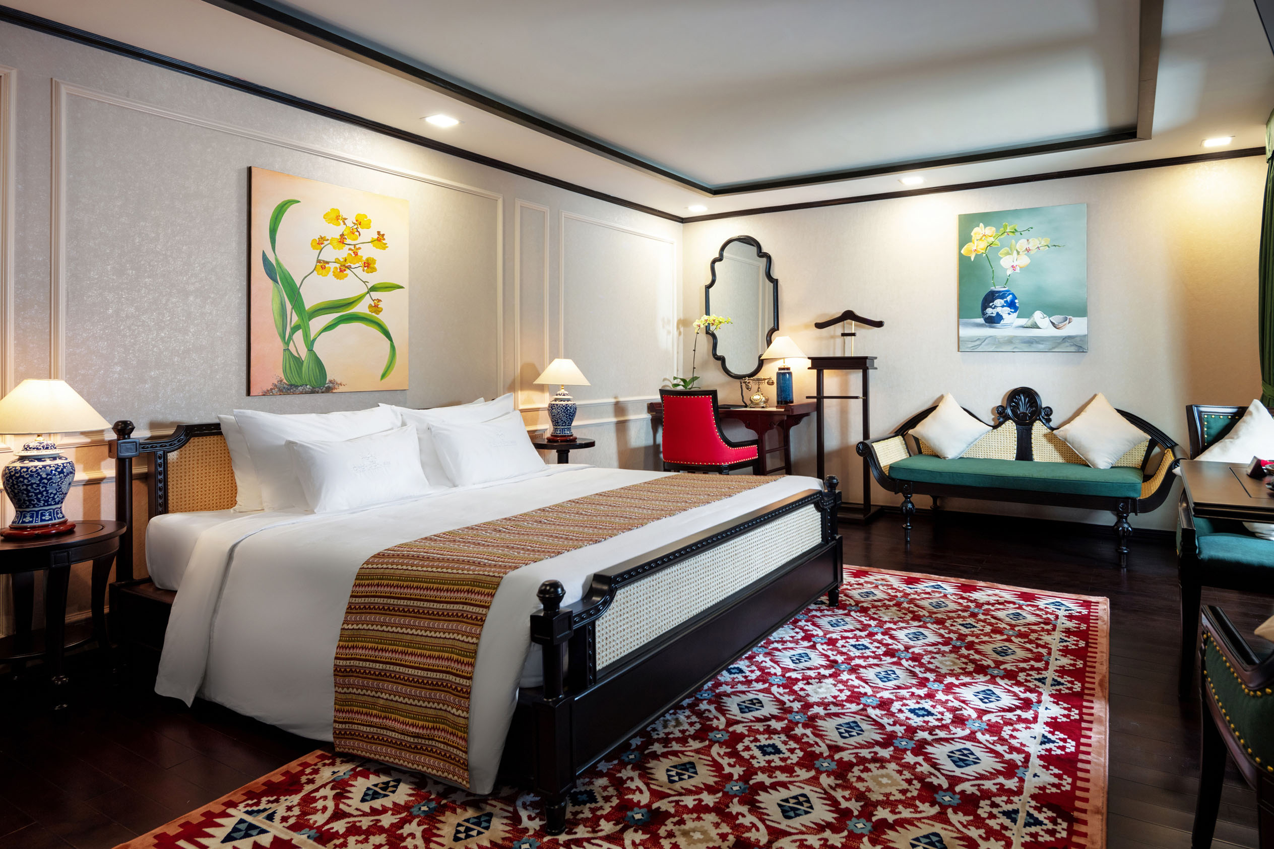 Elegant hotel bedroom with traditional decor, vibrant paintings, and cozy seating area, perfect for a relaxing stay.
