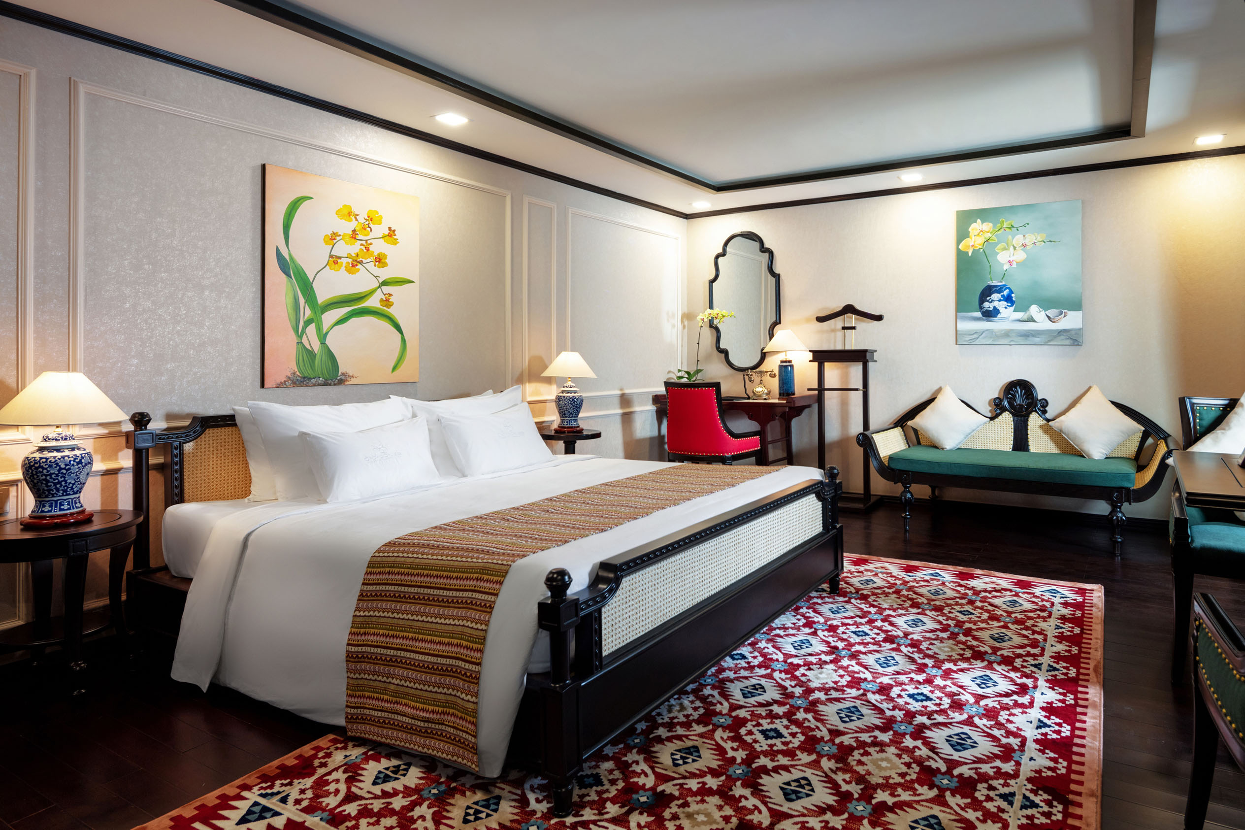 Elegant luxury hotel room with classic decor, floral paintings, and cozy seating area.