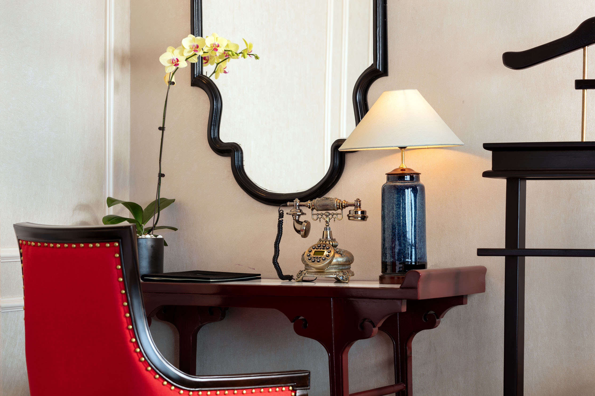 Vintage telephone on elegant wooden desk with lamp and mirror, stylish hotel room decor.