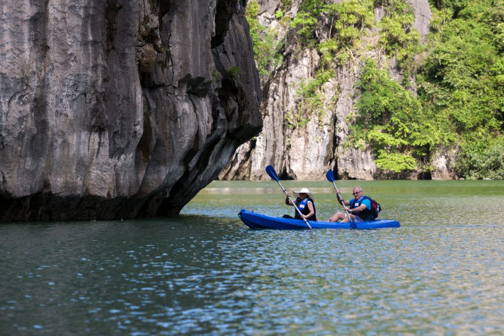 Kayakers exploring scenic limestone cliffs in Vietnam's tranquil waters.