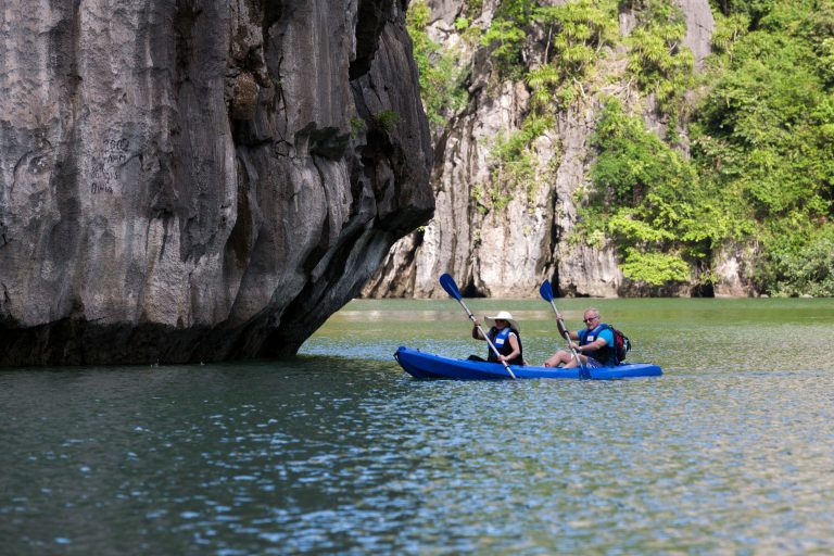 Kayakers exploring scenic limestone cliffs in Vietnam's tranquil waters.