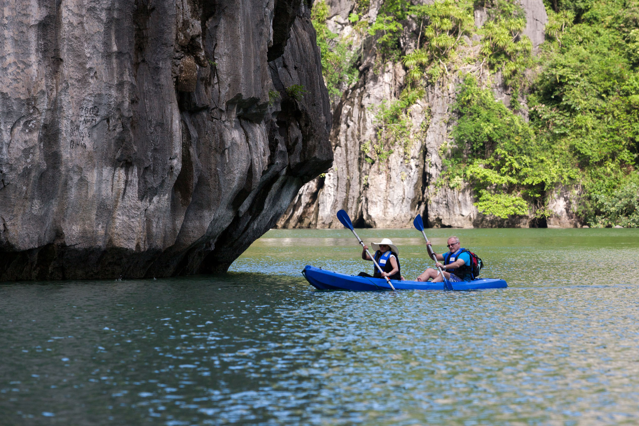 Kayakers exploring scenic limestone cliffs in Vietnam's tranquil waters.