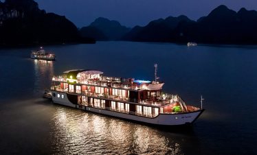 Luxury Orchid cruises ship on Halong Bay at night with illuminated decks and scenic mountain backdrop.