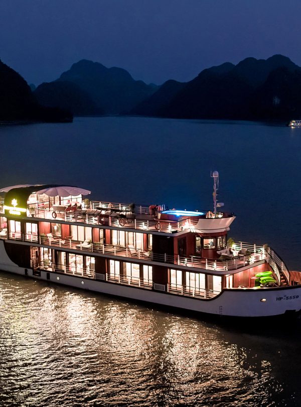 Luxury Orchid cruises ship on Halong Bay at night with illuminated decks and scenic mountain backdrop.