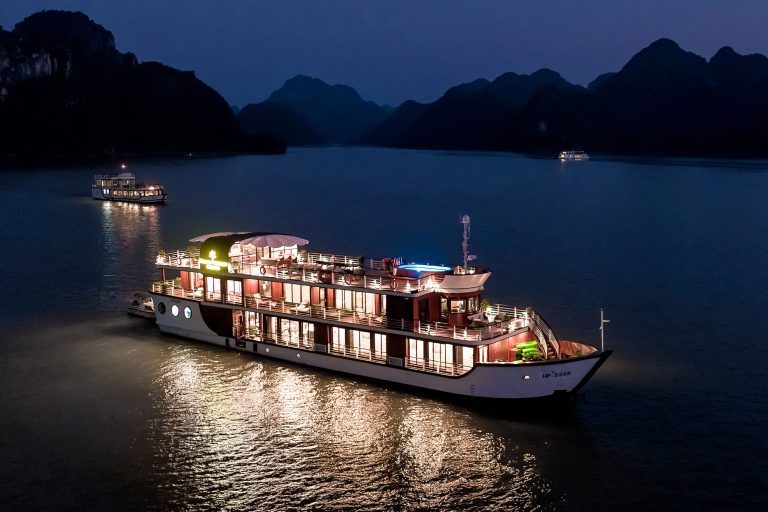 Luxury Orchid cruises ship on Halong Bay at night with illuminated decks and scenic mountain backdrop.