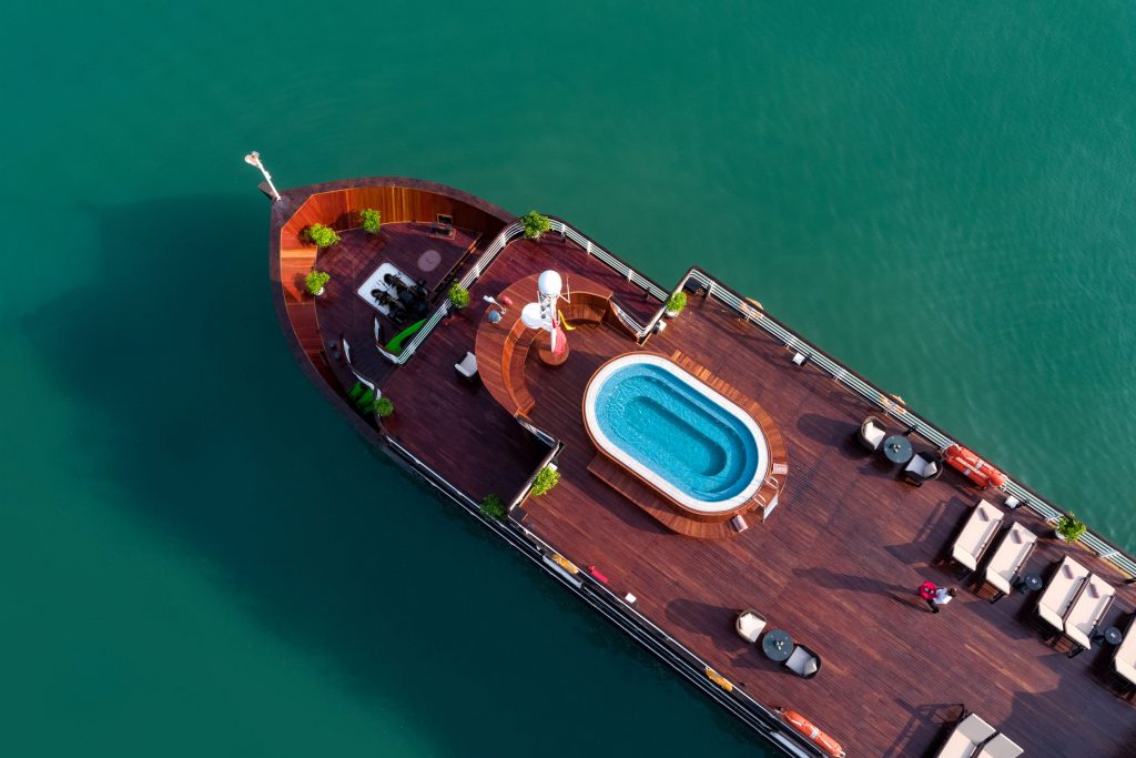 Aerial view of luxury cruise ship with pool, deck, and seating area on calm water, perfect for Vietnam travel.