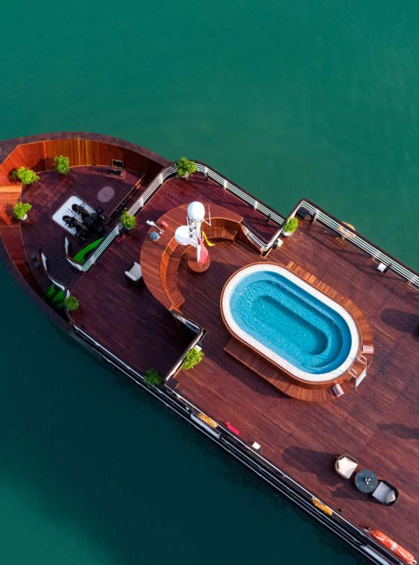 Aerial view of luxury cruise ship with pool, deck, and seating area on calm water, perfect for Vietnam travel.