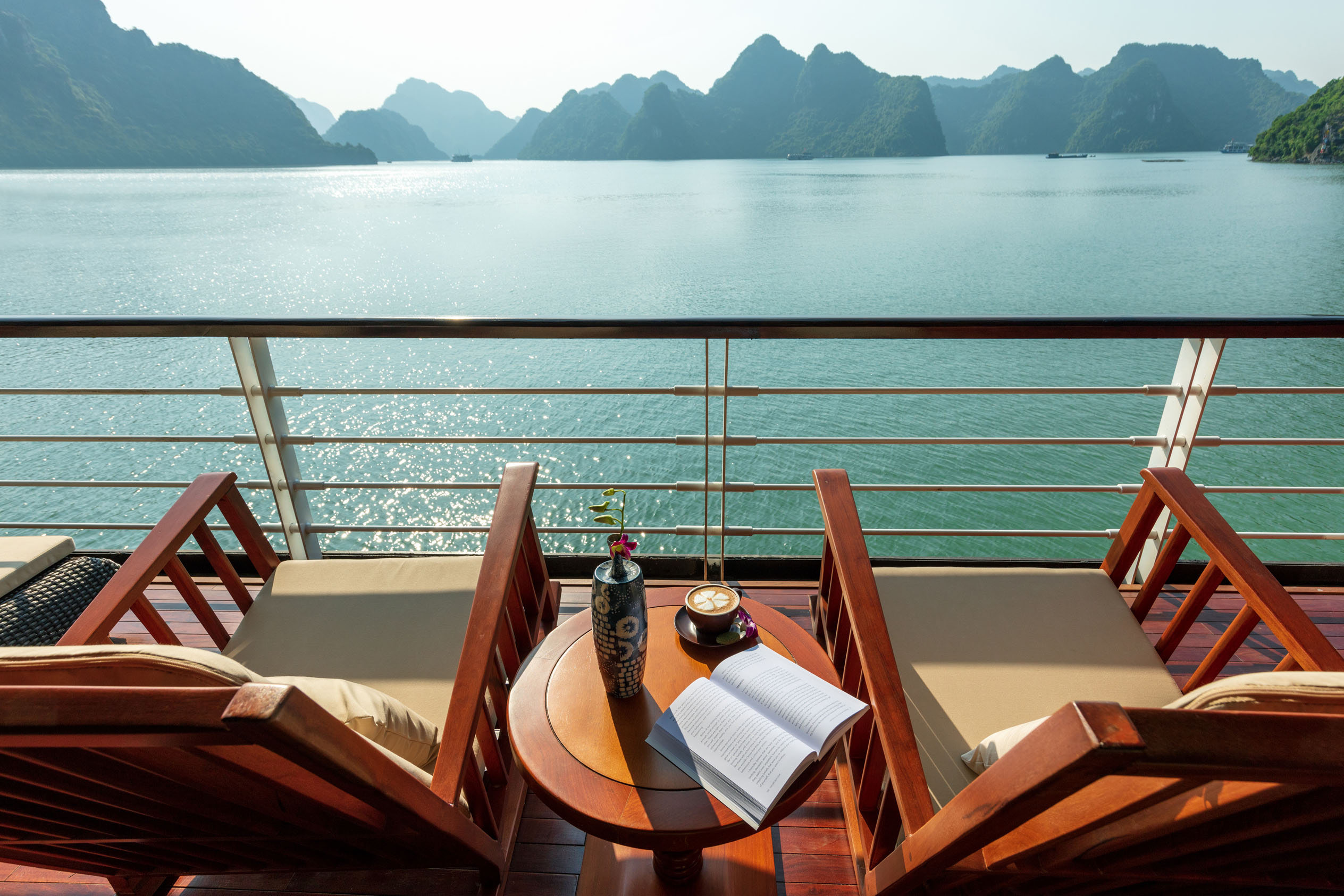 Stunning view of Halong Bay from a cruise balcony with chairs, table, and relaxing ambiance.