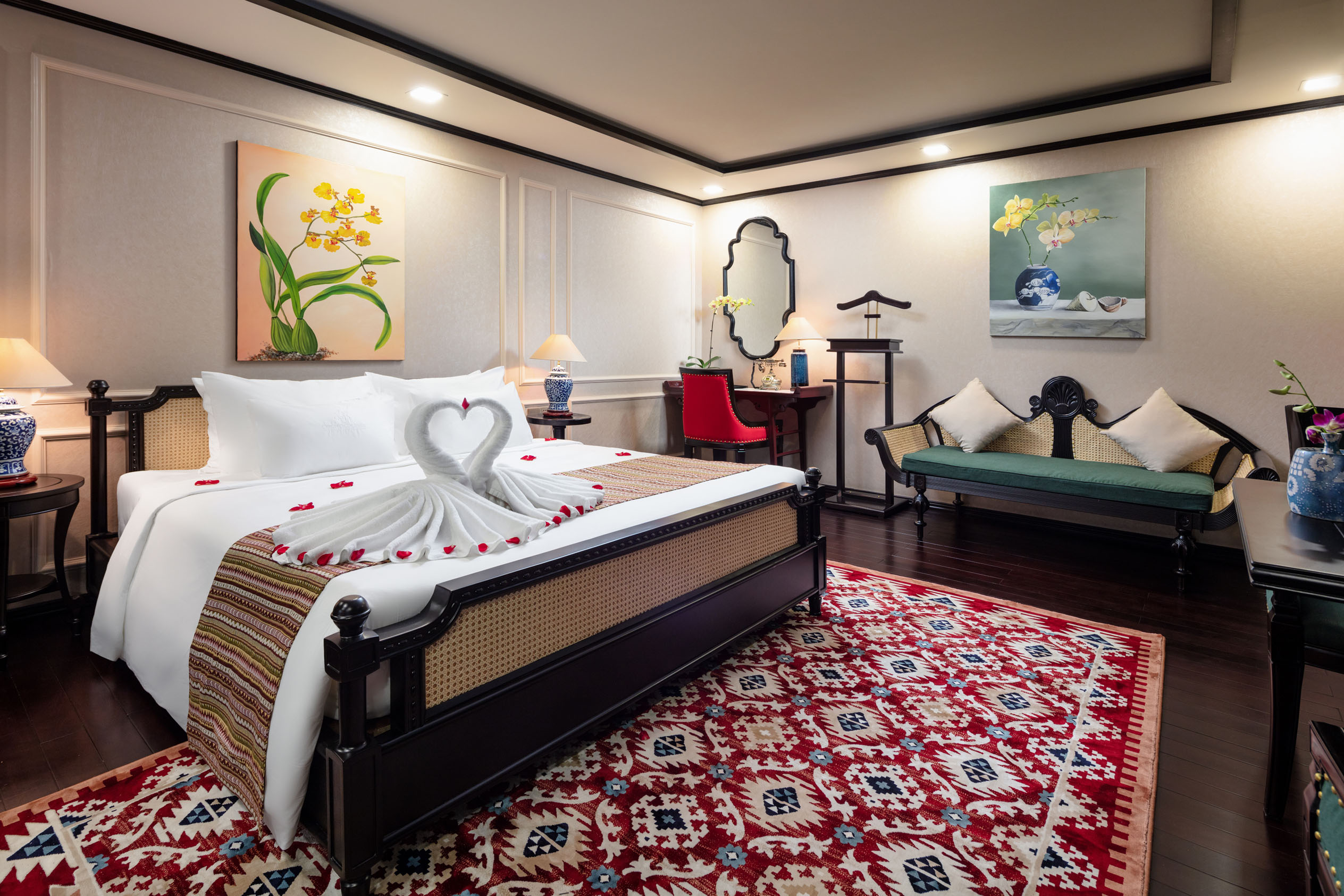 Elegant hotel bedroom with decorative towels, floral artwork, and cozy seating for a luxurious stay.