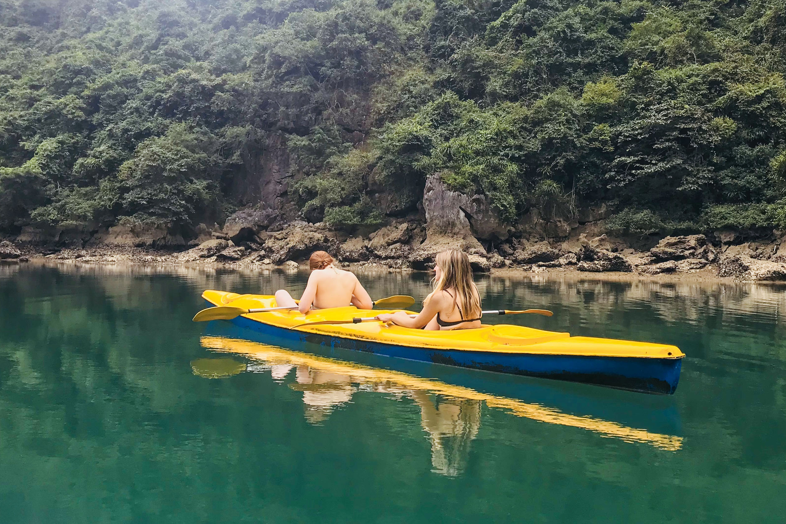 Women kayaking in calm green water surrounded by lush forest, Vietnam travel adventure.