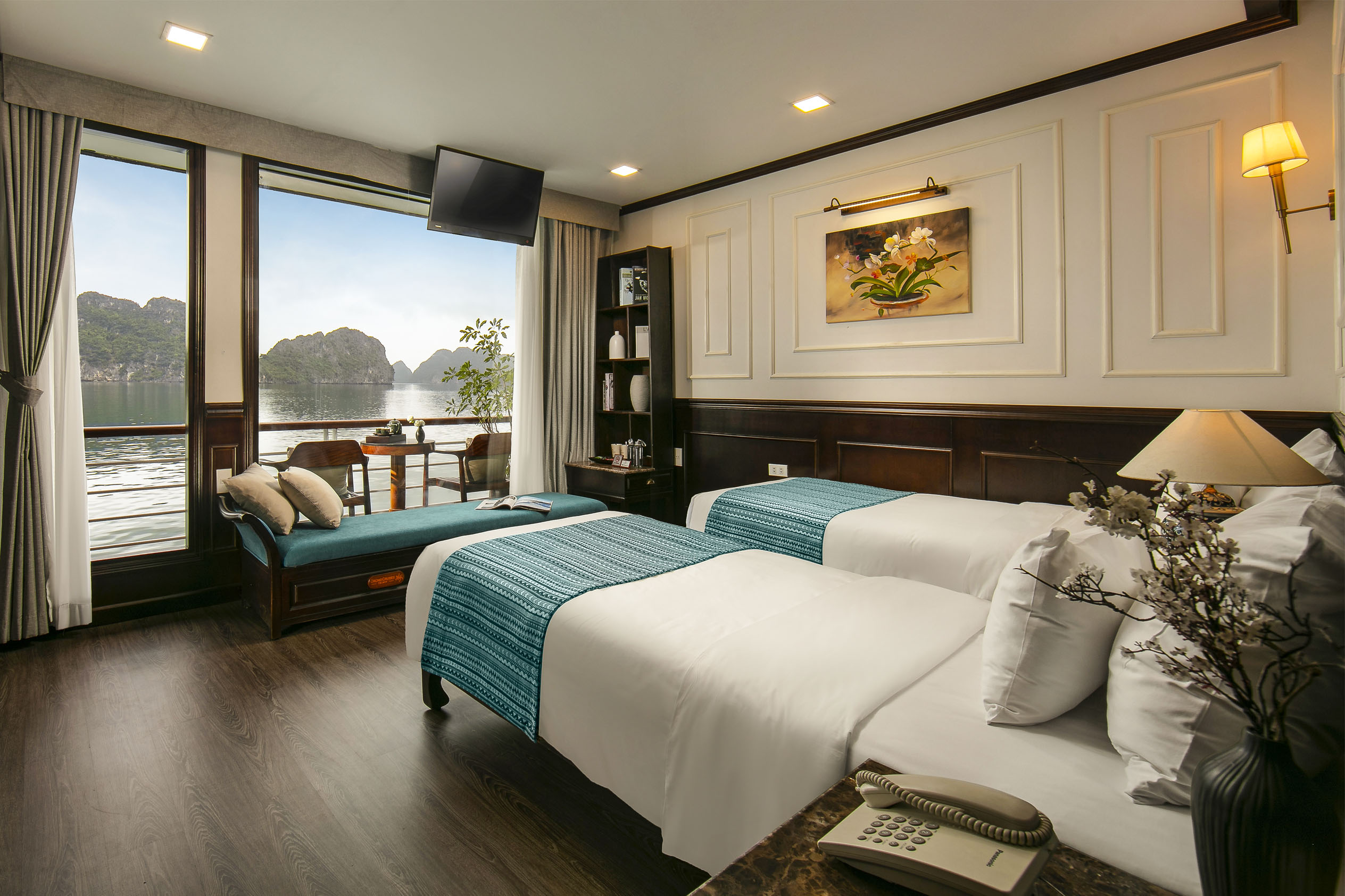 Elegant hotel room with river view, featuring twin beds, a balcony, and scenic limestone island scenery.