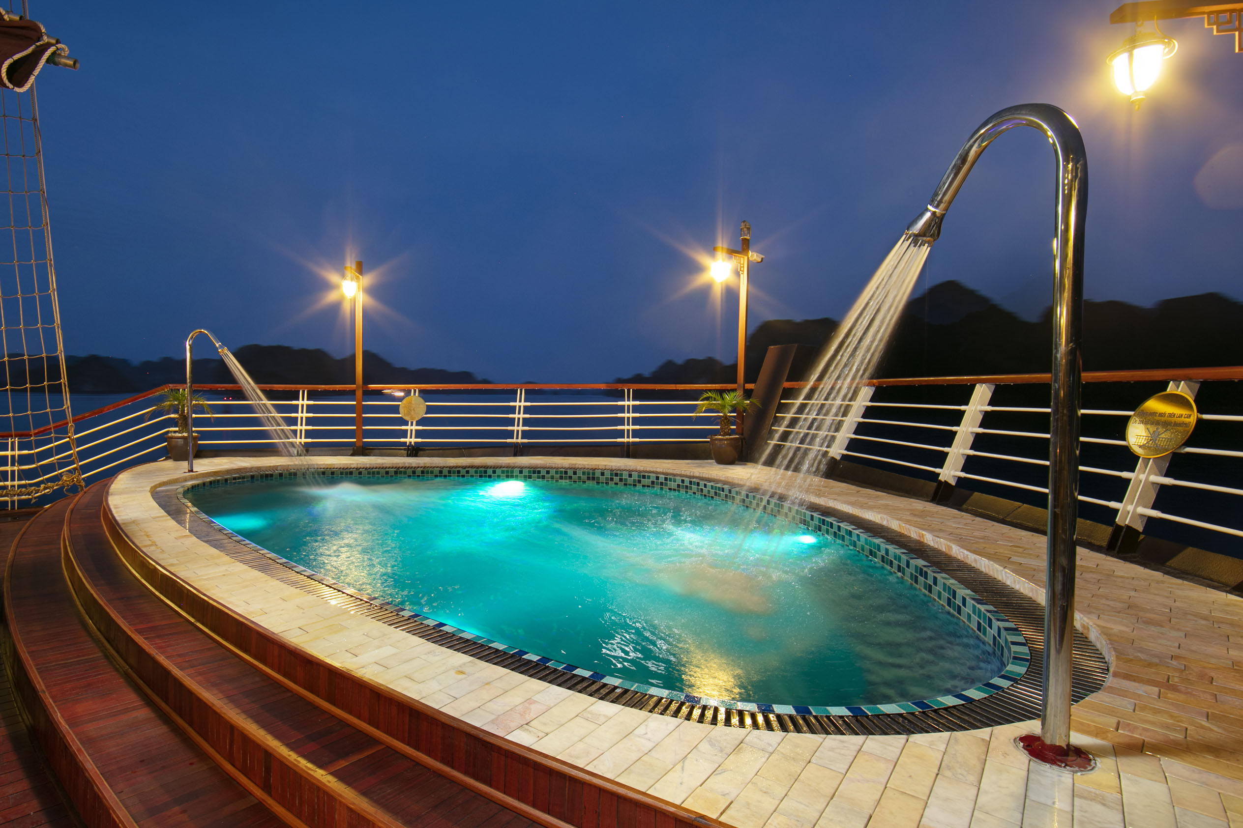 Outdoor hot tub on a cruise ship deck with scenic mountain backdrop at dusk.
