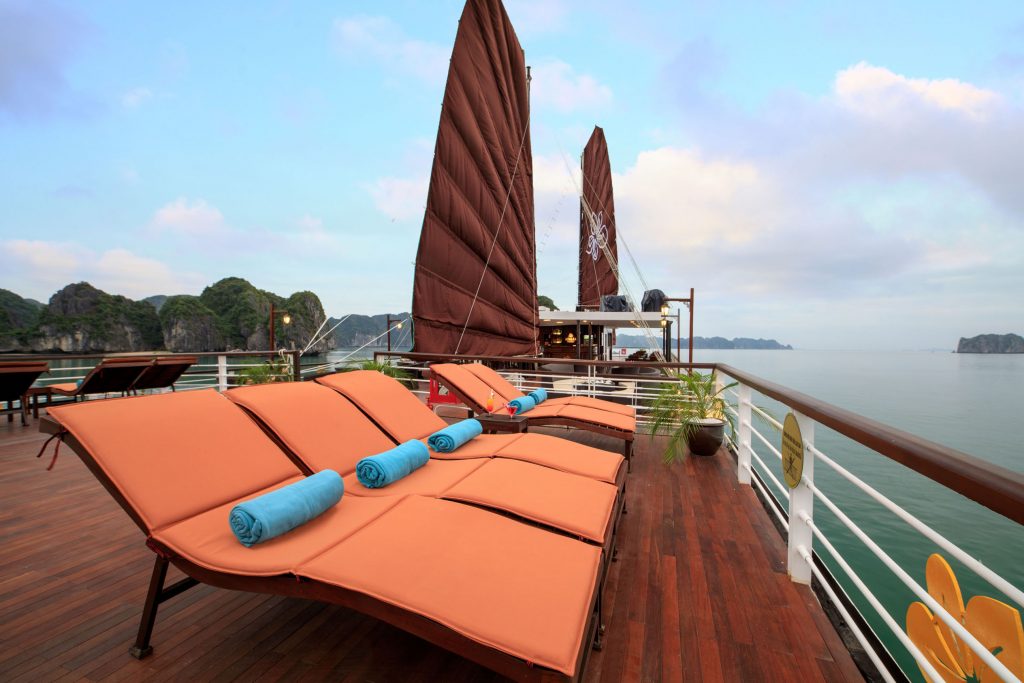 Relaxing boat cruise deck with sun loungers and scenic limestone islands in Vietnam.