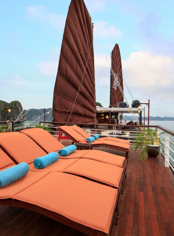 Relaxing boat cruise deck with sun loungers and scenic limestone islands in Vietnam.