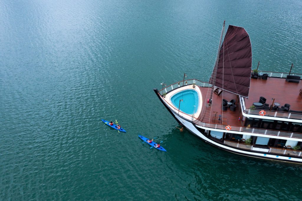 Luxury cruise boat with private pool and kayak on emerald water in Ha Long Bay.