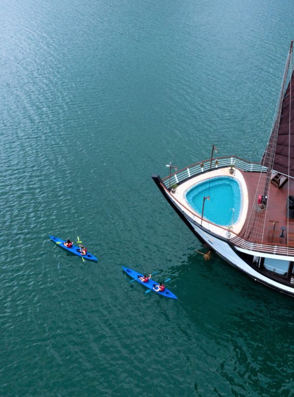 Luxury cruise boat with private pool and kayak on emerald water in Ha Long Bay.