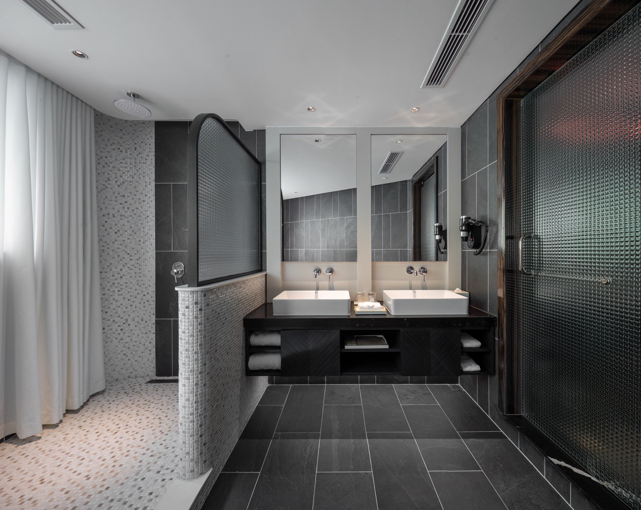 Luxurious modern bathroom with dual sinks, sleek black tiles, and premium amenities.