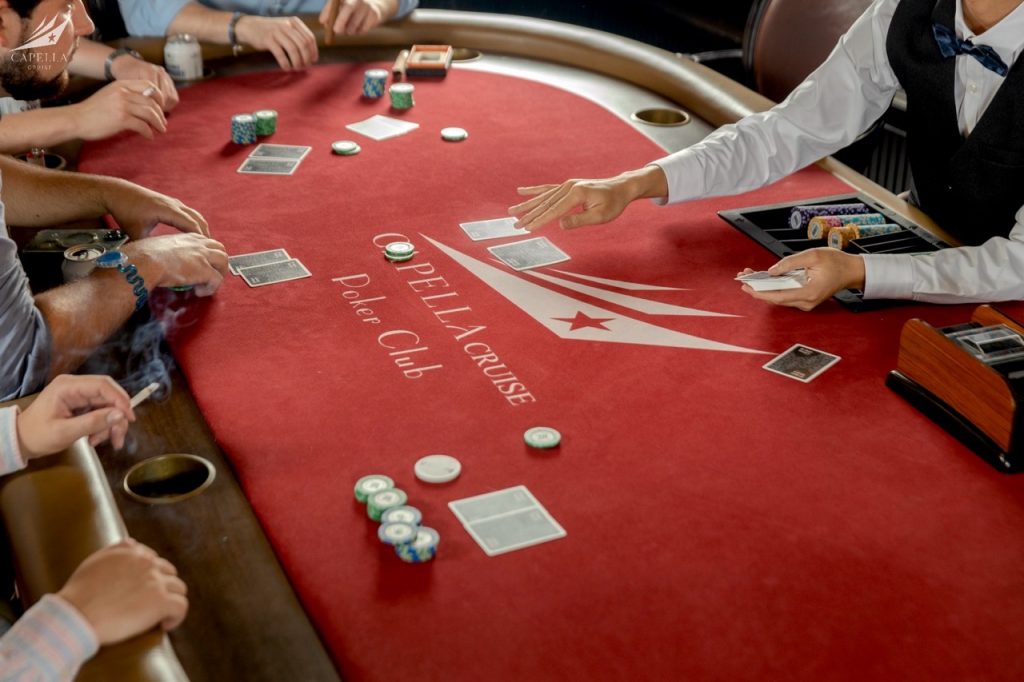 Exciting poker game at Delance Cruise Poker Club with players and dealer on a red felt table.