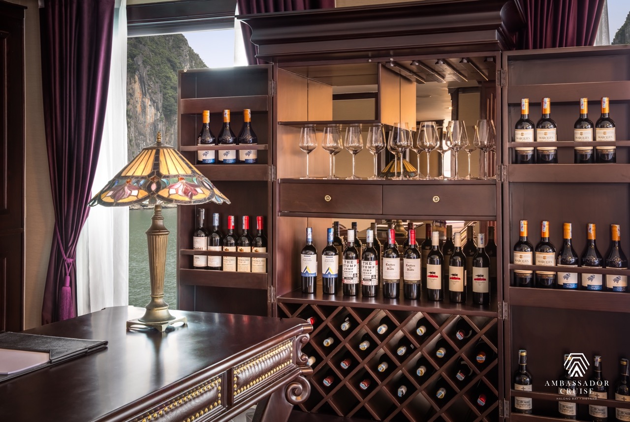 Elegant cruise lounge with wine bottles and glasses overlooking Halong Bay scenery.