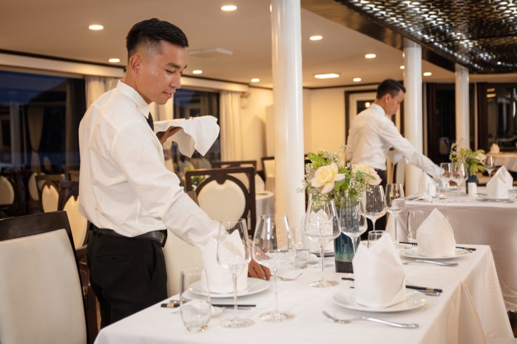 Elegant restaurant setting with waiters preparing tables for fine dining experience.