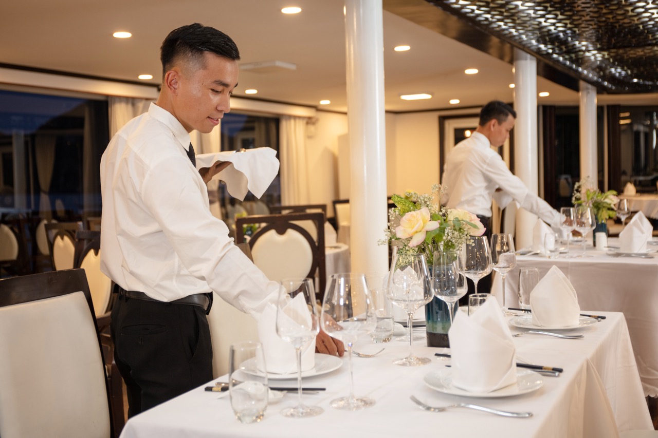 Elegant restaurant setting with waiters preparing tables for fine dining experience.