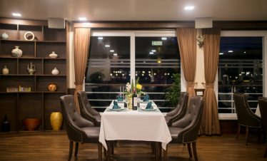 Elegant dining setup on a cruise balcony overlooking Halong Bay at night, with a beautifully set tab.