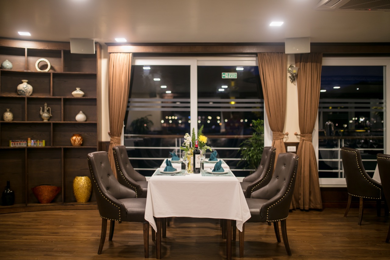 Elegant dining setup on a cruise balcony overlooking Halong Bay at night, with a beautifully set tab.