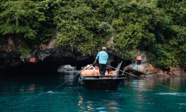 Scenic view of a cruise boat navigating through the emerald waters of Halong Bay, surrounded by lush.