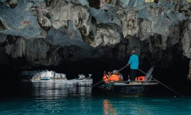 Exploring a stunning cave in Halong Bay on a boat, with dramatic rock formations and calm waters, pe.