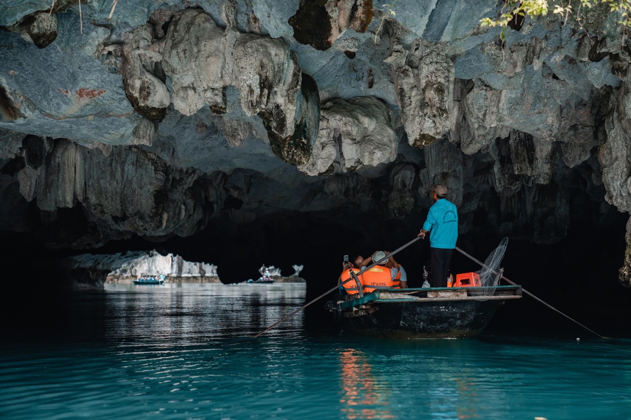 Exploring a stunning cave in Halong Bay on a boat, with dramatic rock formations and calm waters, pe.