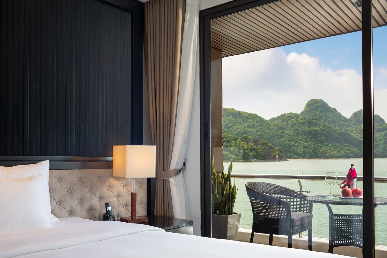 Luxury hotel room with balcony overlooking scenic water and green mountains.