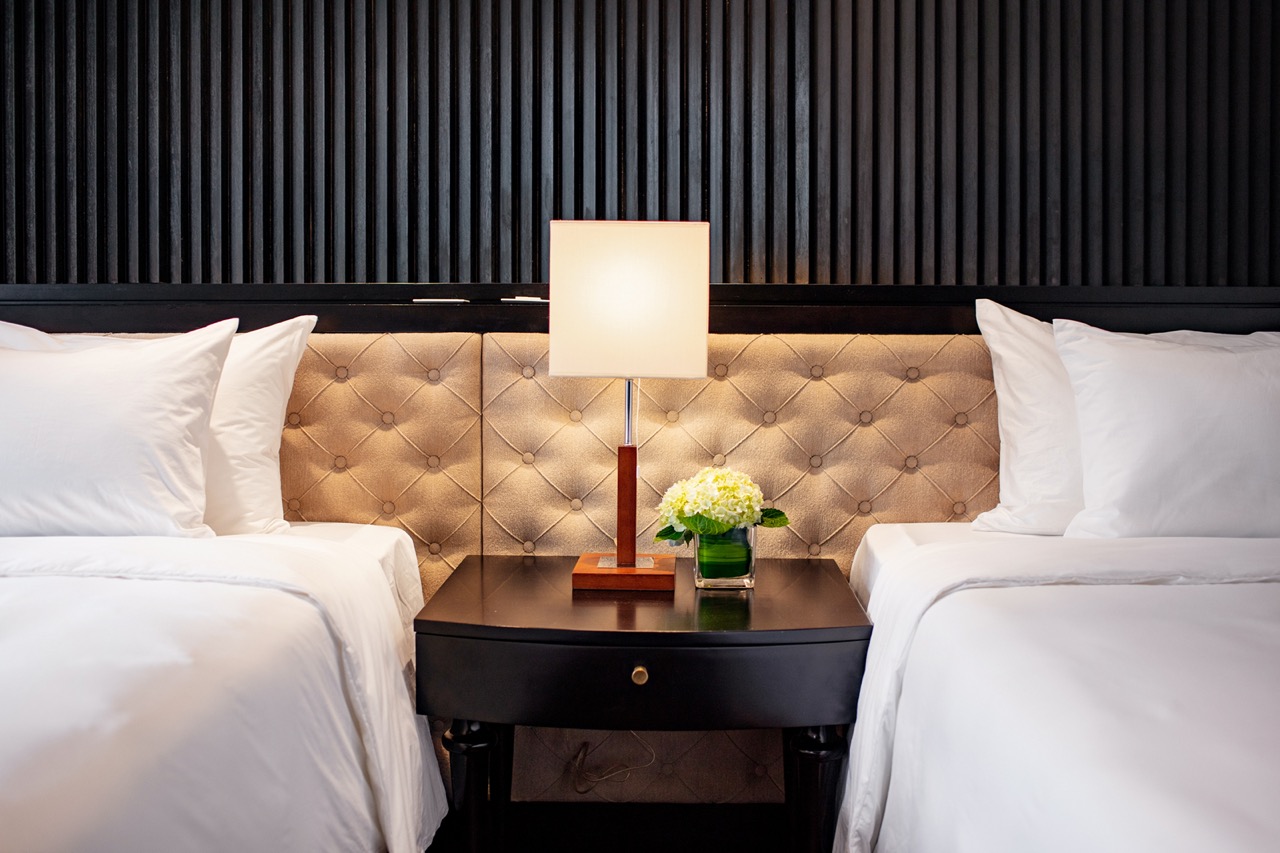 Elegant hotel bedroom with twin beds, bedside lamp, and modern decor for a luxurious stay.
