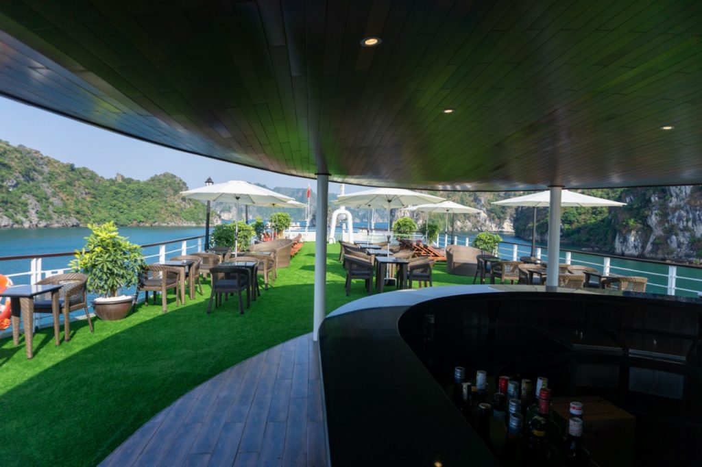 Stunning view of Halong Bay from cruise balcony with outdoor seating and lush greenery.