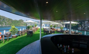 Stunning view of Halong Bay from cruise balcony with outdoor seating and lush greenery.