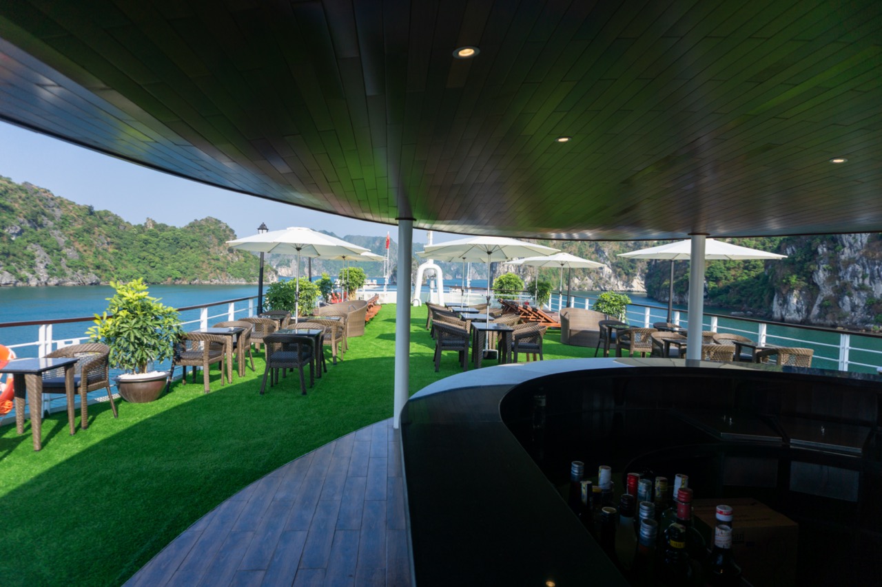 Stunning view of Halong Bay from cruise balcony with outdoor seating and lush greenery.