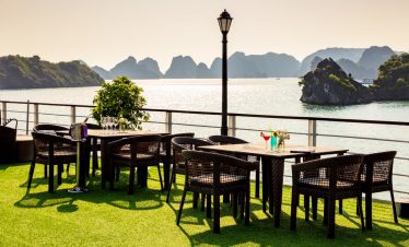 Scenic view of Halong Bay from a cruise balcony with outdoor dining setup and lush islands in the ba.