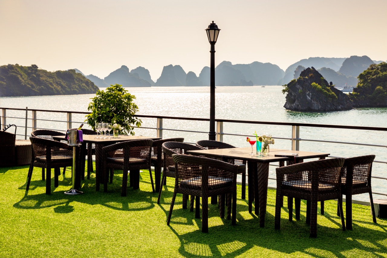 Scenic view of Halong Bay from a cruise balcony with outdoor dining setup and lush islands in the ba.