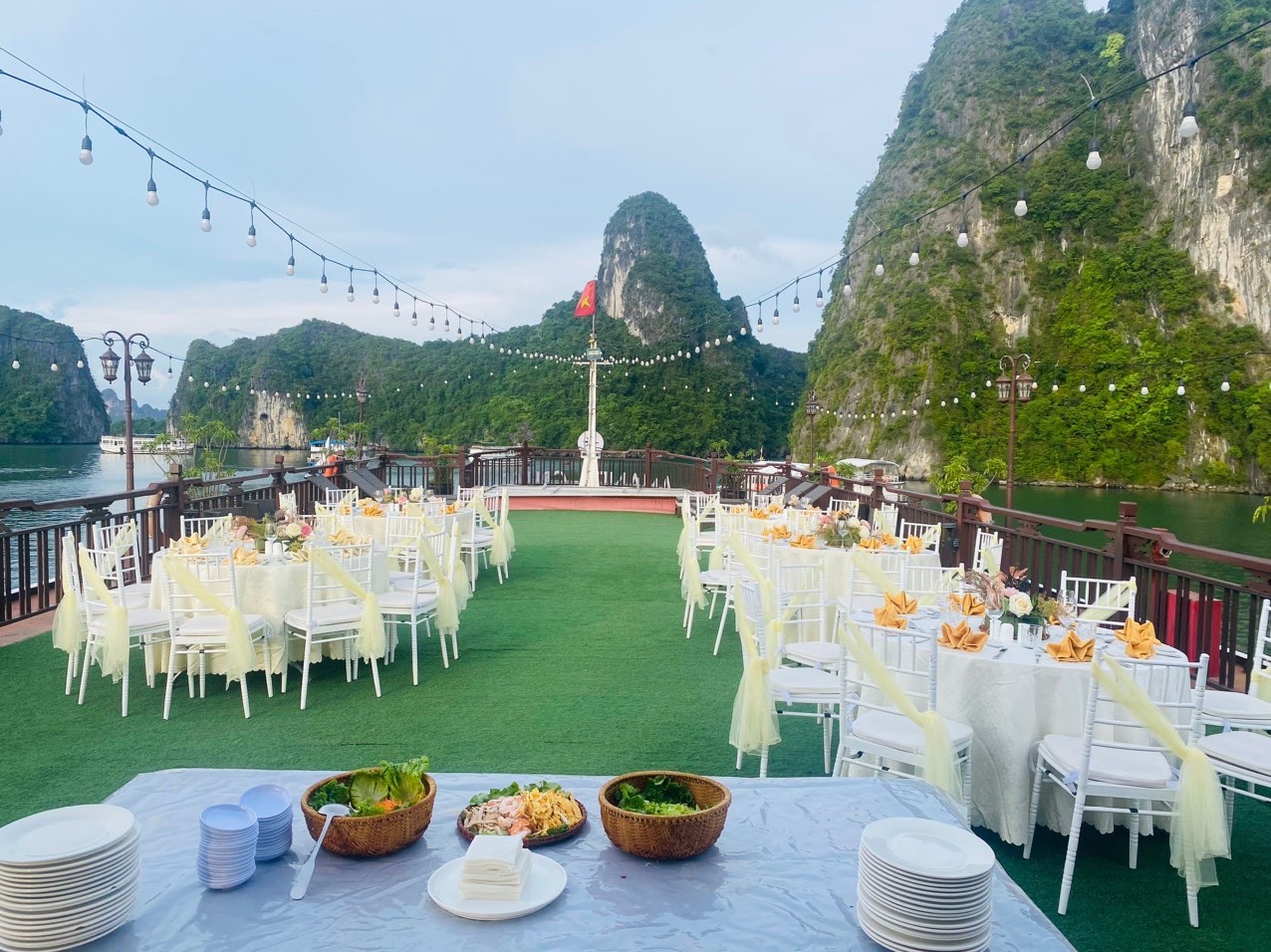 Lakeside boat dinner with elegant tables, string lights, and scenic limestone mountains in Vietnam.