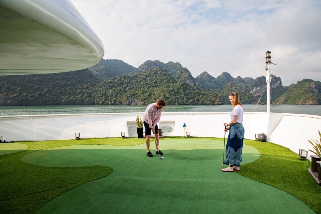 Victorian-style cruise ship enjoying a scenic golf session on deck with mountain views.