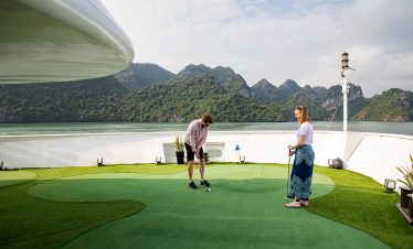 Victorian-style cruise ship enjoying a scenic golf session on deck with mountain views.