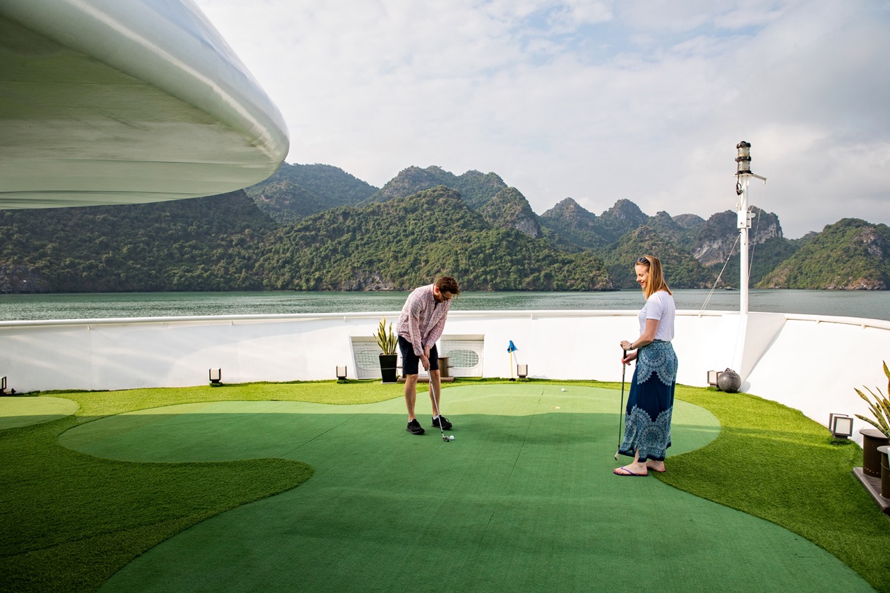 Victorian-style cruise ship enjoying a scenic golf session on deck with mountain views.