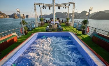 Scenic view of a luxury cruise deck with hot tub, overlooking Halong Bay's limestone islands and cal.